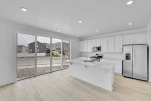 Kitchen featuring appliances with stainless steel finishes, white cabinetry, light wood-style floors, a kitchen island with sink, and recessed lighting