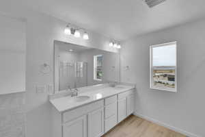 Bathroom featuring double vanity, a stall shower, and light wood-style floors