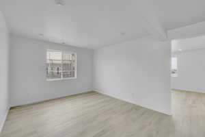 Unfurnished room featuring light wood-style flooring and beamed ceiling