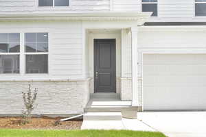 View of exterior entry with concrete driveway, a garage, and stone siding