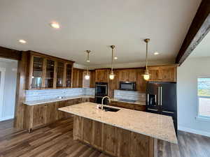 Kitchen with glass insert cabinets, an island with sink, dark wood-style floors, decorative backsplash, and decorative light fixtures