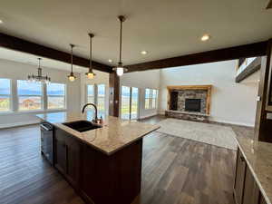 Kitchen featuring beamed ceiling, decorative light fixtures, dark brown cabinets, light stone countertops, and open floor plan