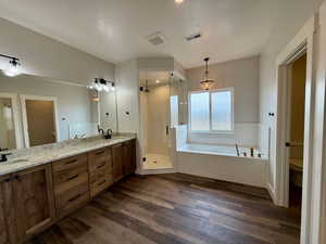 Full bathroom with a shower stall, double vanity, a garden tub, and dark wood finished floors