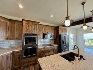 Kitchen featuring hanging light fixtures, black appliances, decorative backsplash, recessed lighting, and light stone counters