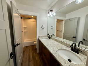 Full bathroom with dark wood finished floors, double vanity, and bathtub / shower combination