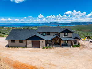 View of front of home with dirt driveway, a shingled roof, a garage, and a water and mountain view
