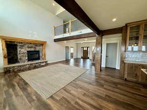 Unfurnished living room with a stone fireplace, beamed ceiling, dark wood-type flooring, and recessed lighting