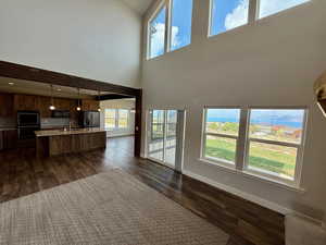Unfurnished living room with dark wood-type flooring, healthy amount of natural light, and a towering ceiling