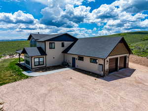 View of front facade featuring driveway, roof with shingles, stone siding, and central AC