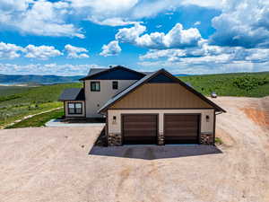 View of front facade with stone siding, dirt driveway, board and batten siding, a garage, and a mountain view