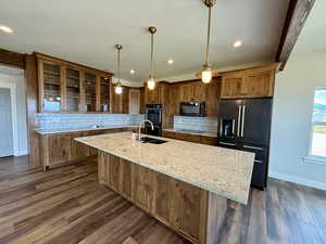 Kitchen with black appliances, glass insert cabinets, a center island with sink, light stone counters, and recessed lighting