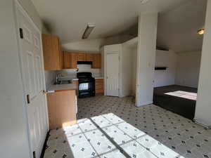 Kitchen featuring light floors, a sink, light countertops, lofted ceiling, and black range with electric cooktop