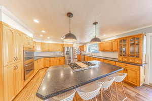 Kitchen with light wood finished floors, decorative light fixtures, a breakfast bar area, a kitchen island, and appliances with stainless steel finishes