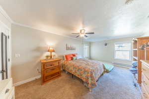 Bedroom with light colored carpet, multiple windows, a ceiling fan, a textured ceiling, and a baseboard heating unit
