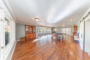 Game room featuring wood-type flooring, french doors, a barn door, ornamental molding, and a textured ceiling