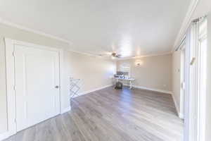Unfurnished living room featuring crown molding, light wood-style floors, ceiling fan, and a desk