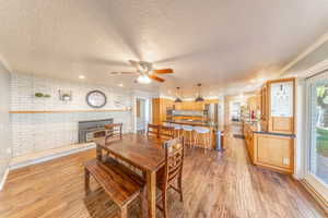 Dining room with ornamental molding, light wood finished floors, brick wall, ceiling fan, and a textured ceiling