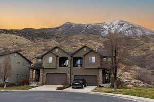 View of front of house with a mountain view, stone siding, a garage, and stucco siding