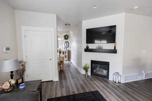 Living room featuring visible vents, a large fireplace, baseboards, and wood finished floors