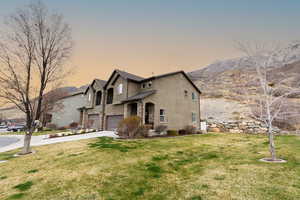 View of front of property with stucco siding, a mountain view, driveway, an attached garage, and a yard