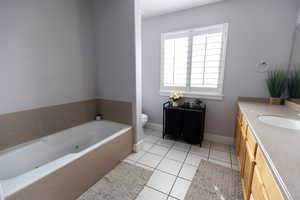 Bathroom with baseboards, toilet, a tub with jets, vanity, and tile patterned floors