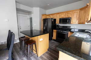 Kitchen featuring dark wood-style floors, a center island, stainless steel gas range oven, black refrigerator with ice dispenser, and a sink