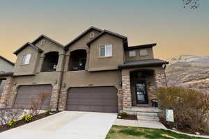 View of front of home with a garage, stucco siding, stone siding, a mountain view, and concrete driveway