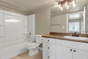 Bathroom with a textured ceiling, toilet, vanity, shower / bath combination, and tile patterned flooring