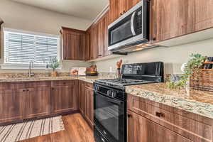 Kitchen featuring light stone counters, a sink, wood finished floors, stainless steel microwave, and black range with gas cooktop