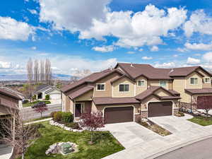 View of front of home featuring concrete driveway, stucco siding, fence, roof with shingles, and stone siding