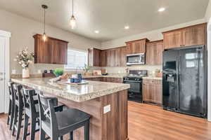 Kitchen with pendant lighting, a breakfast bar area, a peninsula, light wood-style flooring, and black appliances