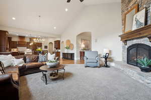 Living room featuring high vaulted ceiling, a stone fireplace, arched walkways, ceiling fan with notable chandelier, and light colored carpet