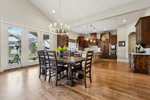 Dining area with an inviting chandelier, arched walkways, high vaulted ceiling, and wood flooring