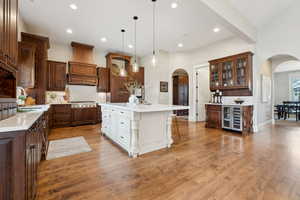 Kitchen featuring light countertops, stainless steel gas cooktop, a sink, arched walkways, and custom exhaust hood