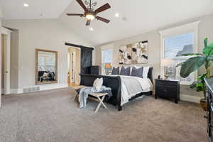 Bedroom featuring visible vents, a ceiling fan, light carpet, a barn door, and vaulted ceiling