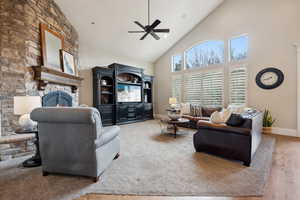 Living room featuring a ceiling fan, a stone fireplace, high vaulted ceiling, and huge windows with mountain views.
