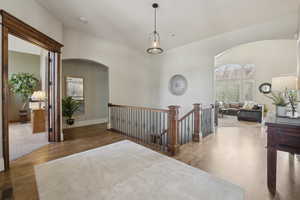 Hallway with arched walkways, visible vents, wood floors, an upstairs landing