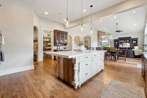 Kitchen with glass insert cabinets, light countertops, arched walkways, and light wood-style floors