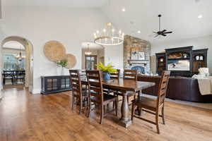 Dining area featuring high vaulted ceiling, arched walkways, ceiling fan with notable chandelier, and light wood-style floors