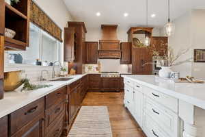 Kitchen featuring light countertops, stainless steel gas cooktop, premium range hood, a sink, and wood finished floors