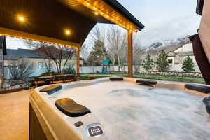 View of covered patio with a hot tub, a mountain view, fence and a playset.