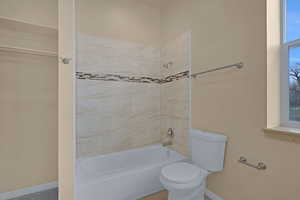 Full bath featuring washtub / shower combination, baseboards, and toilet