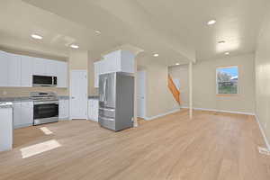 Kitchen featuring light wood-type flooring, baseboards, white cabinets, and stainless steel appliances