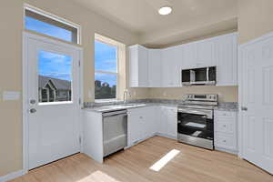 Kitchen with stainless steel appliances, light wood finished floors, white cabinets, and light stone counters