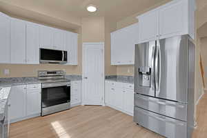 Kitchen with light wood finished floors, white cabinets, and stainless steel appliances