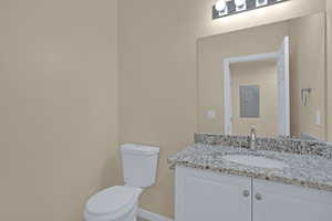 Half bathroom with electric panel, vanity, baseboards, and toilet