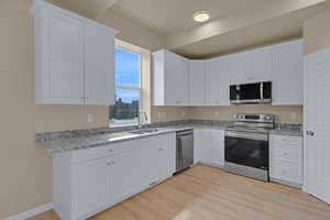Kitchen featuring light wood-type flooring, appliances with stainless steel finishes, a sink, and white cabinetry
