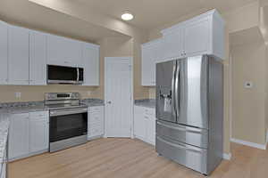 Kitchen with baseboards, light wood-type flooring, appliances with stainless steel finishes, white cabinetry, and light stone countertops