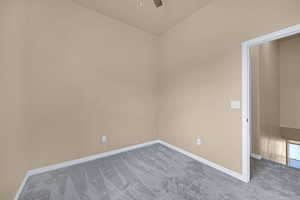 Carpeted spare room featuring baseboards, a ceiling fan, and lofted ceiling