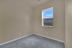 Unfurnished room featuring baseboards, dark colored carpet, a ceiling fan, and visible vents